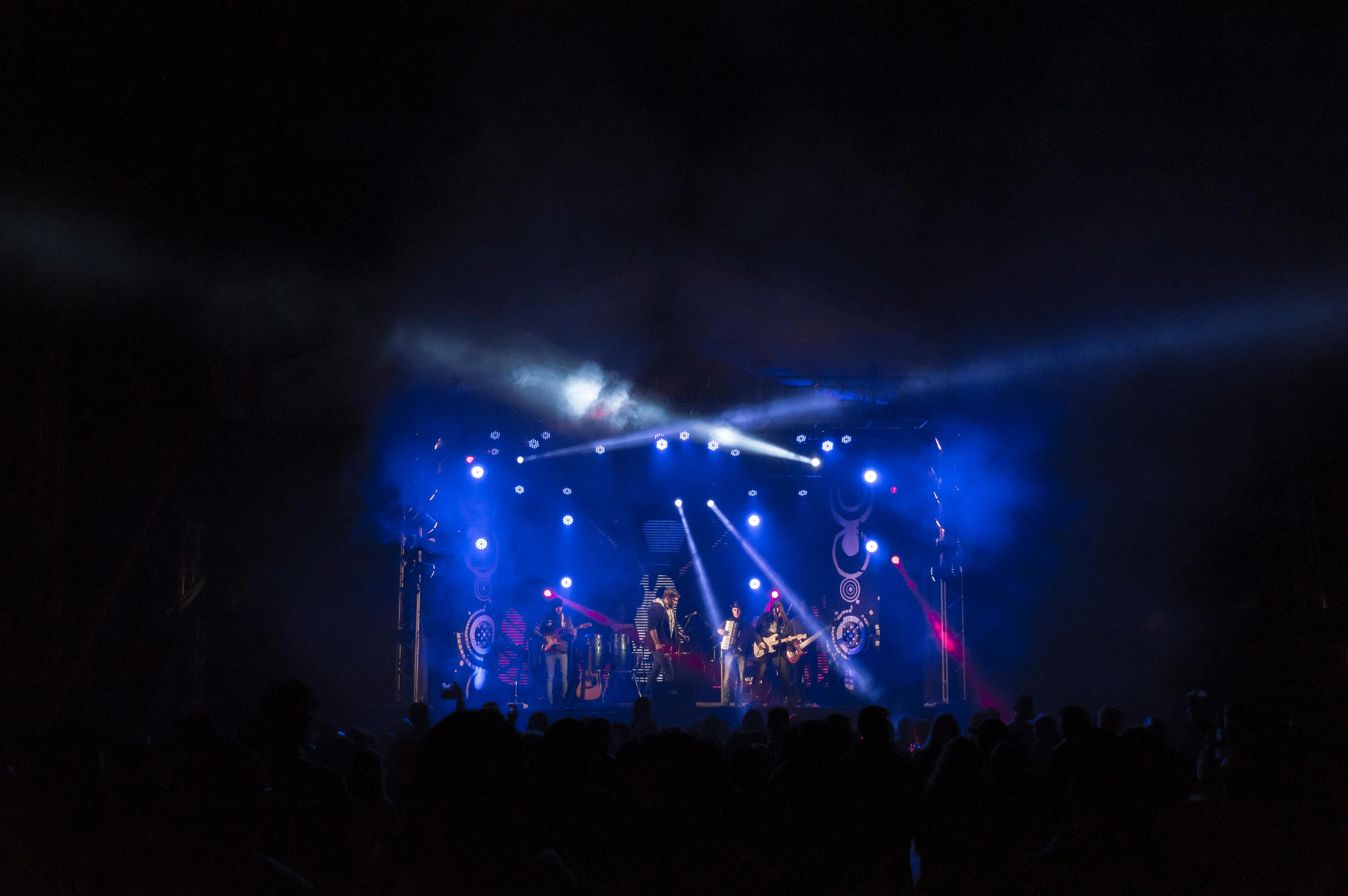 Concierto en un lugar oscuro con luces azules y personas levantando las manos